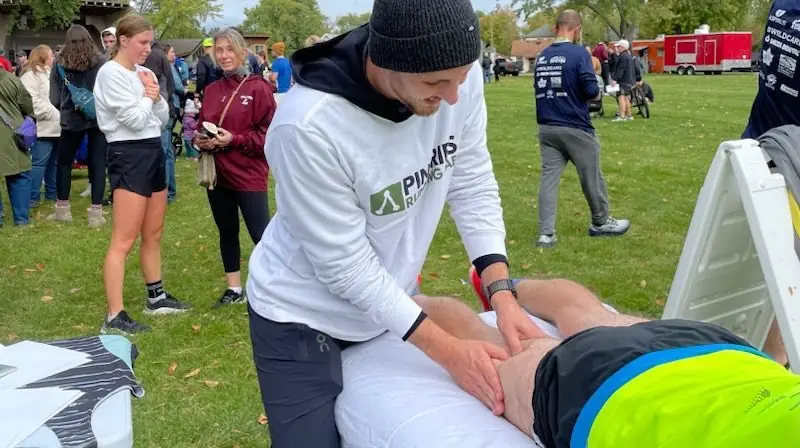 A Pineries Running Lab therapist working on a runner's leg at a community race in the park